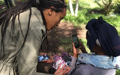 Two women with mobile phones in their hands are talking to each other