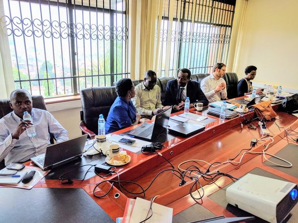 Six peolpe sitting at a big workingtable with notebooks on it, some of them talking to each other