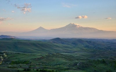 Green hilly landscape and high and snow covered mountains in the background