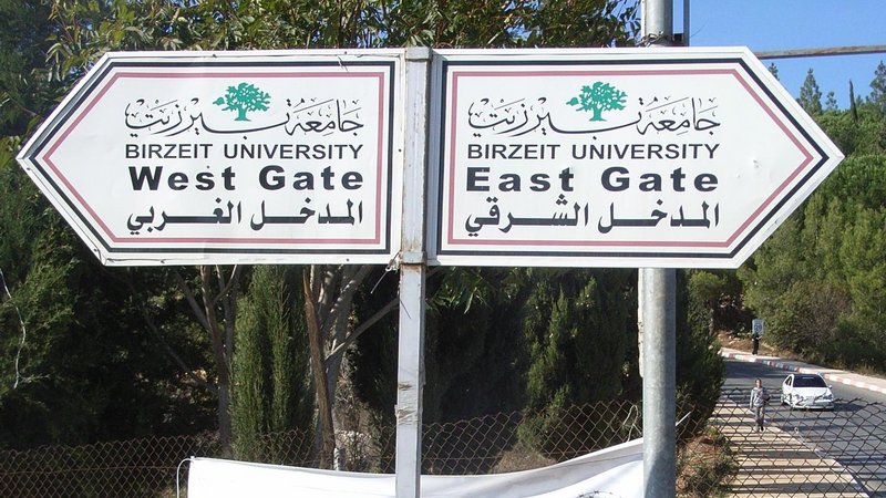 Two signs standing on the roadside in front of a fence