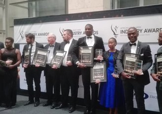 A group of eight people receiving awards, stand in front of a large roll-up announcing the African Utility Week Industry Awards