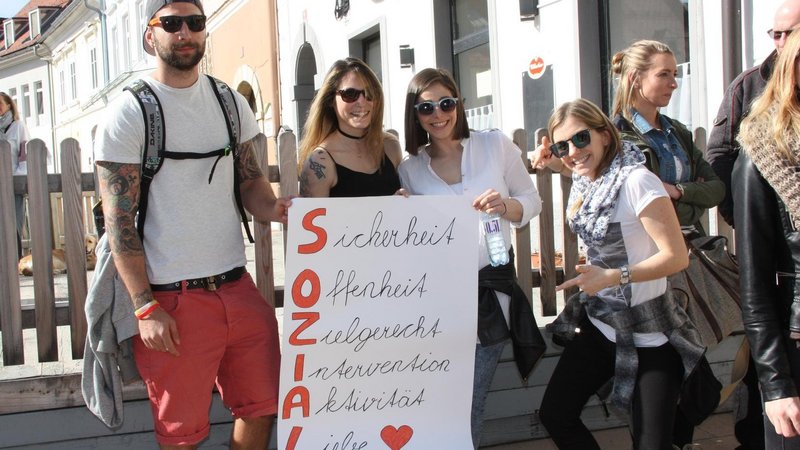 Group of people with sunglasses holding up a poster with a slogan on it