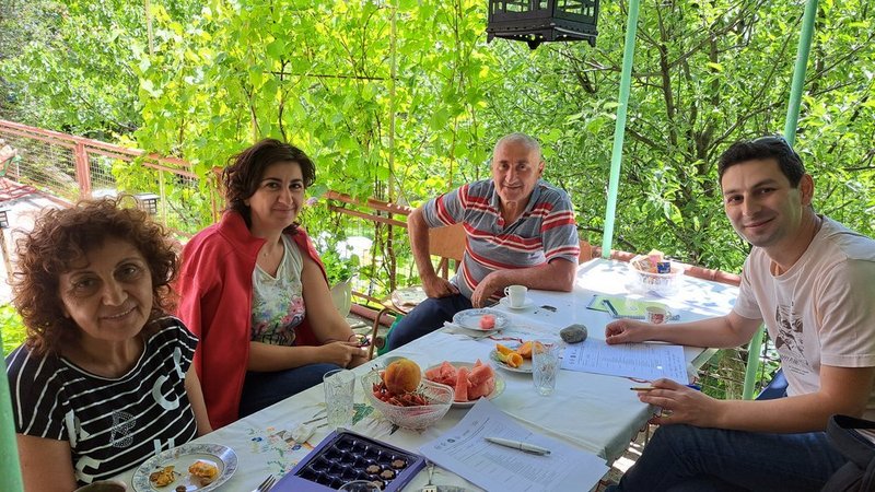 The picture shows Tigran Keryan interviewing 2 women and one man in a garden-like setting in Ddmashen, Armenia